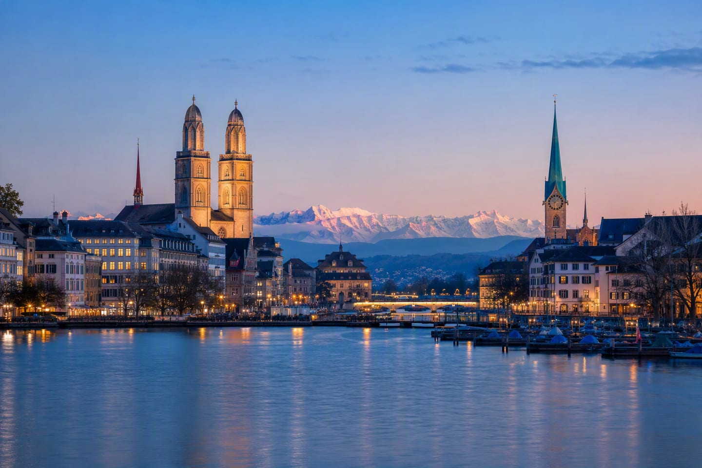 Zurich’s waterfront at blue hour, with the Grossmünster towers and Fraumünster rising above Lake Zurich as the Alps glow faintly on the horizon.