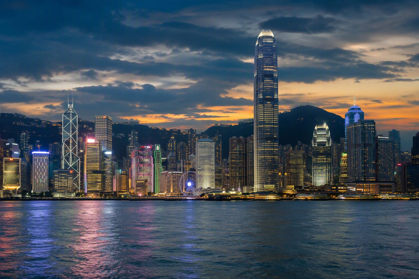 Hong Kong’s Victoria Harbour glows at dusk, with the illuminated skyline of the International Commerce Centre and Bank of China Tower reflected across the water.