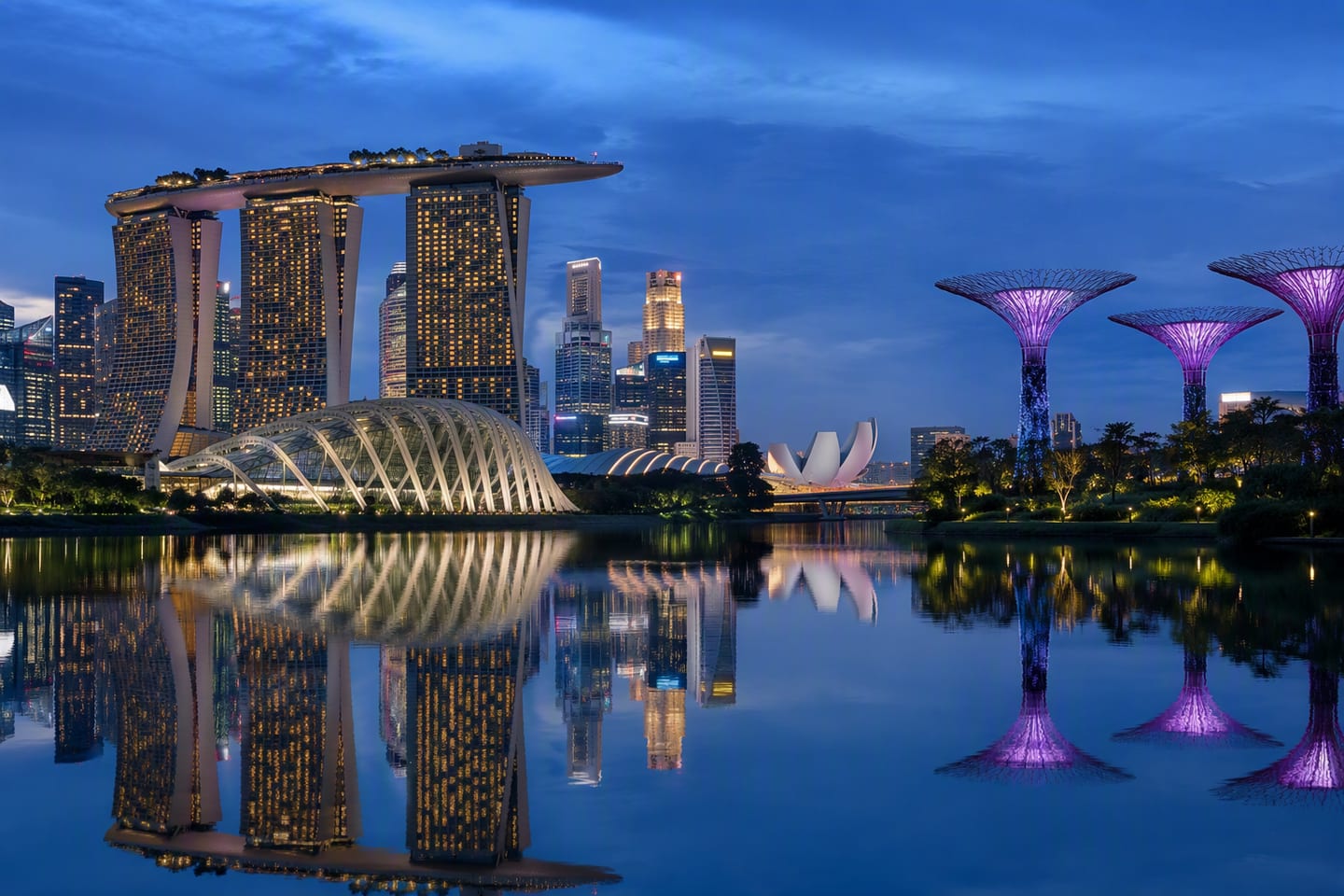 Singapore’s Marina Bay skyline glows at blue hour, with Marina Bay Sands and the illuminated Supertree Grove reflected in the calm waterfront.