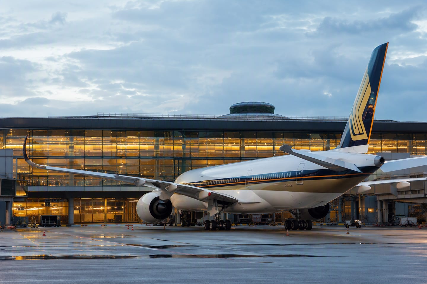 A wide-body Airbus A350 bearing Singapore Airlines’ livery rests at the gate beneath the glowing terminal glass at Singapore Changi Airport.