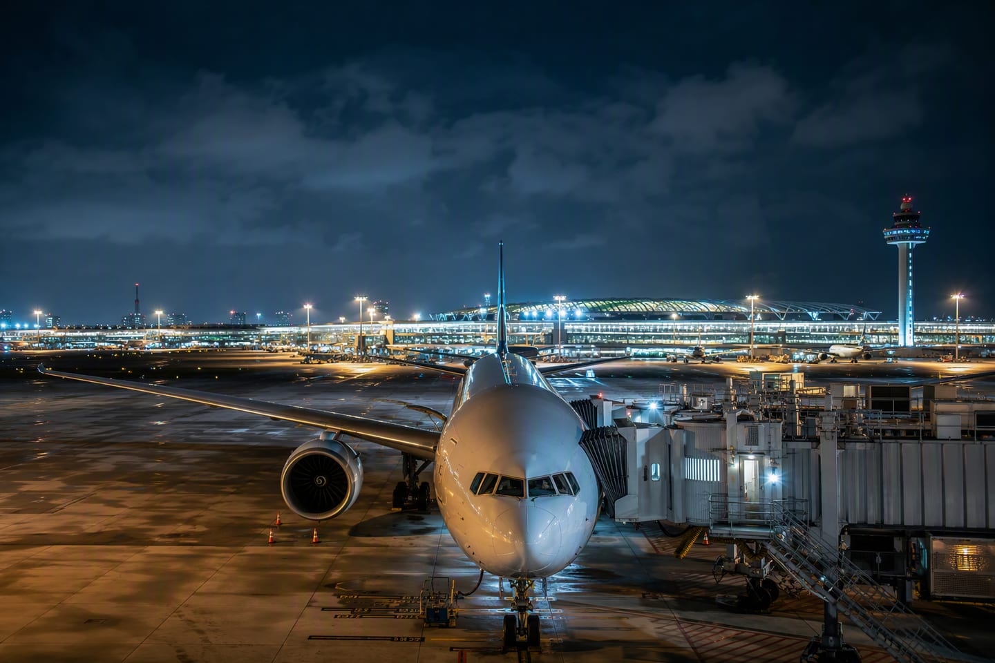 A wide-body Boeing 777 at the gate beneath the glowing night skyline of Singapore’s Changi Airport, its polished fuselage reflecting the terminal lights.