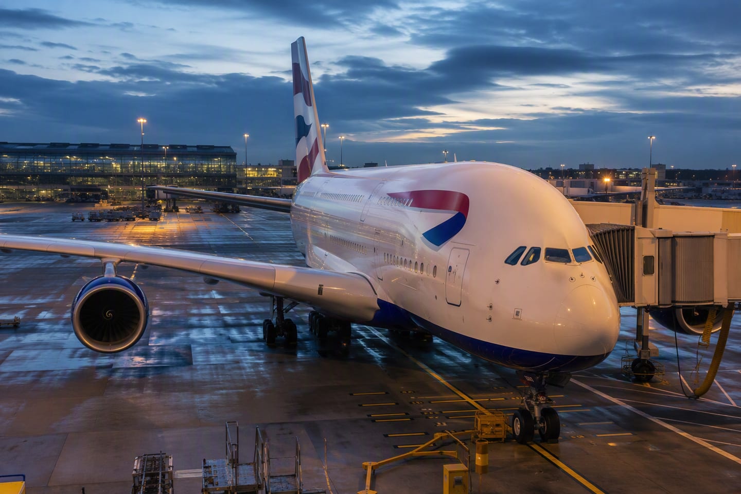 A British Airways Airbus A380 rests at a Heathrow Terminal 5 gate at blue hour, its polished fuselage glowing beneath the airport’s amber lights.
