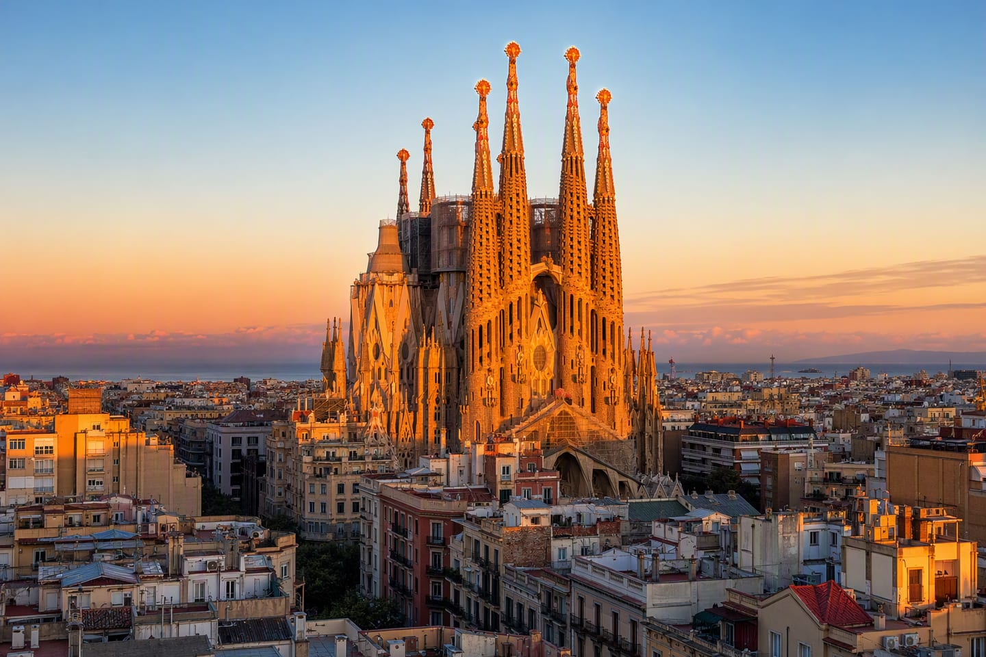 Barcelona’s Sagrada Família rises above the city at golden hour, with its intricate towers glowing against a clear Mediterranean sky.