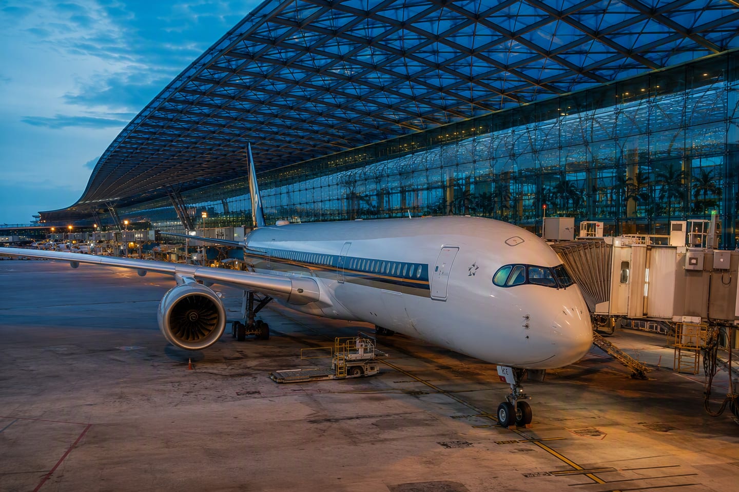A Singapore Airlines Airbus A350 sits at the gate beneath the sweeping glass roof of Singapore Changi Airport’s Terminal 3 at blue hour.