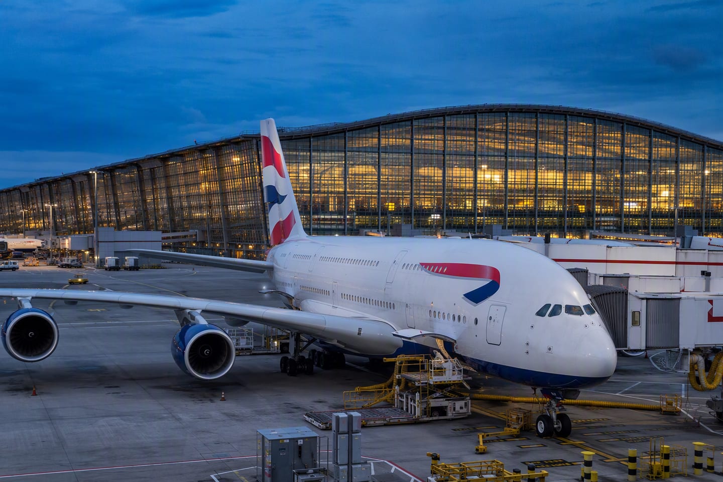 A British Airways Airbus A380 rests at the gate beneath the glowing departure hall of London Heathrow Terminal 5 at blue hour.