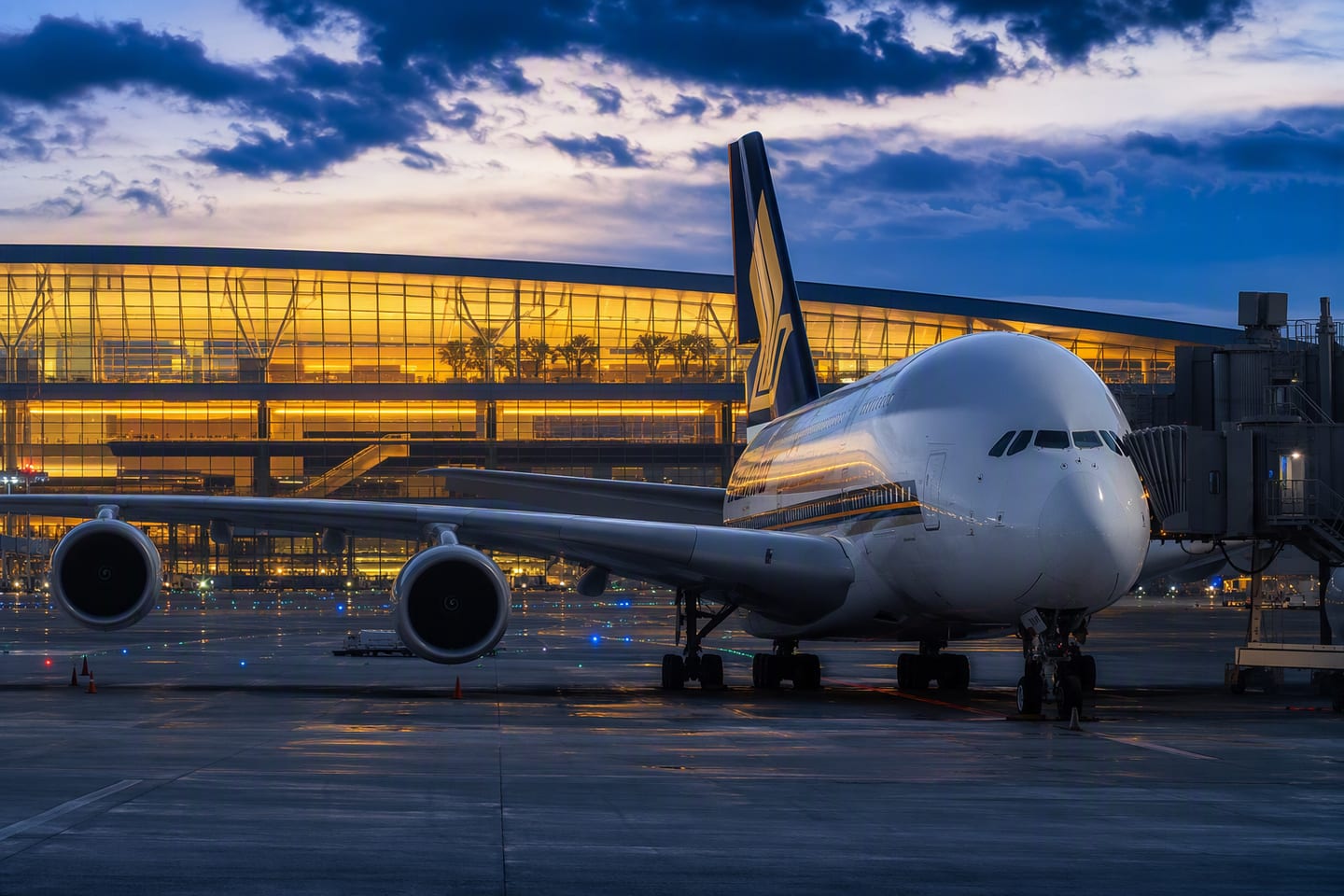 A Singapore Airlines Airbus A380 rests at the gate beneath the glowing departure hall at Singapore Changi Airport, its polished fuselage reflecting the blue-hour runway lights.
