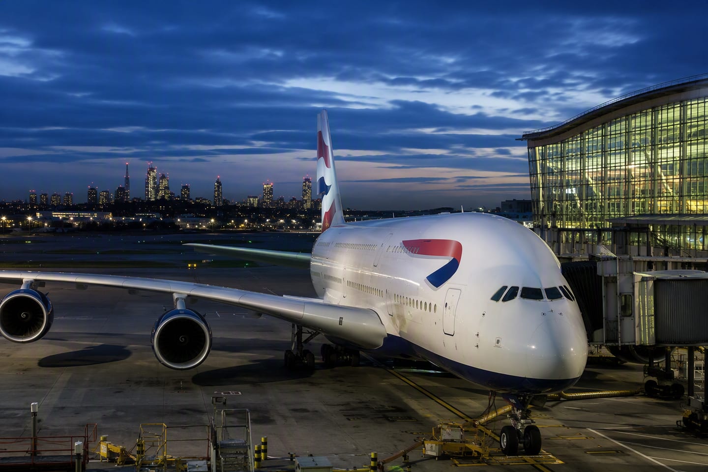 A British Airways Airbus A380 rests at a Heathrow Terminal 5 gate at blue hour, its polished fuselage reflecting the airport’s glowing glass architecture and London’s distant skyline.