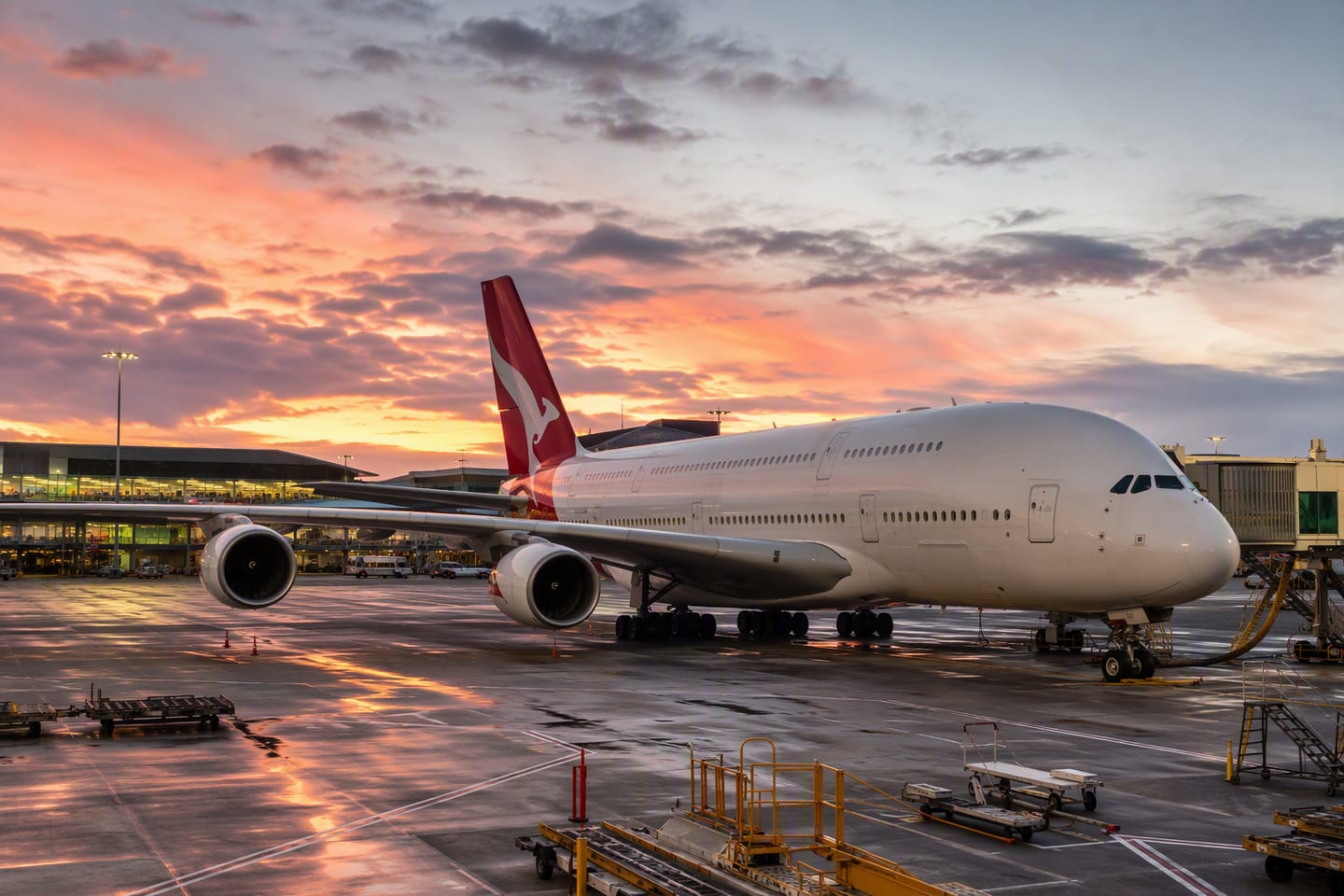 A Qantas Airbus A380 in distinctive red-and-white livery stands at the international terminal gate at Sydney Kingsford Smith Airport beneath a glowing dusk sky, ready for its long-haul journey to Europe.