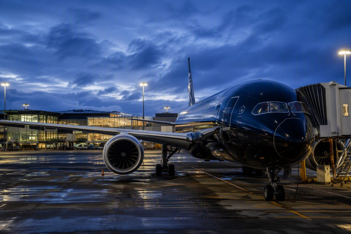 A wide-body Air New Zealand jet rests at its gate at Auckland Airport at blue hour, with the terminal lights glowing against the deepening New Zealand sky.