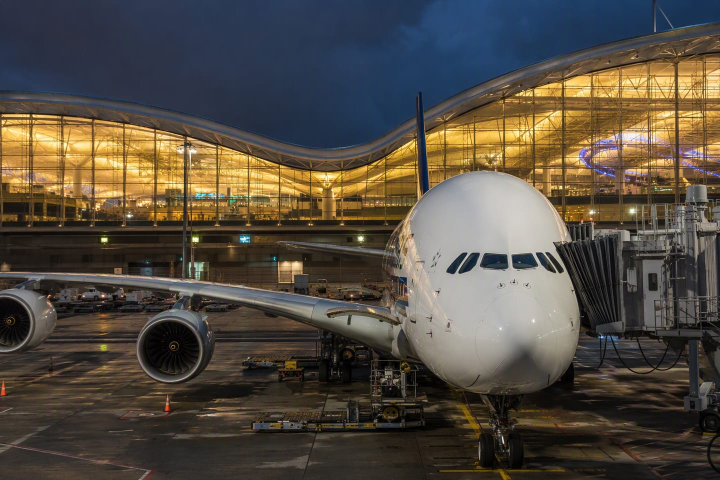 A Singapore Airlines Airbus A380 sits at the gate beneath the glowing departure hall of Singapore Changi Airport, its polished fuselage reflecting the terminal lights.