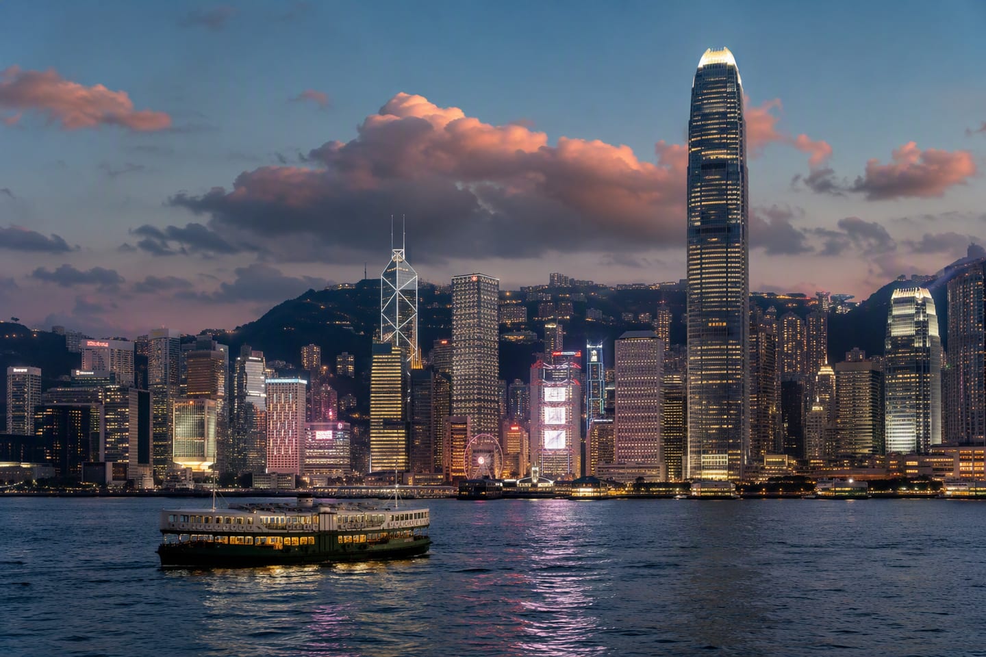 Hong Kong’s Victoria Harbour glows at dusk beneath the illuminated skyline of the International Commerce Centre and Bank of China Tower, with the Star Ferry crossing the calm water in the foreground.