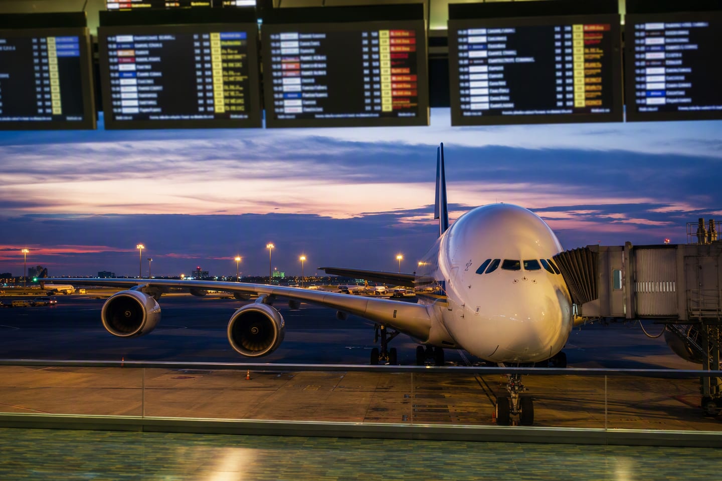 A Singapore Airlines Airbus A380 sits at the gate beneath the illuminated departure boards at Singapore Changi Airport after dusk.