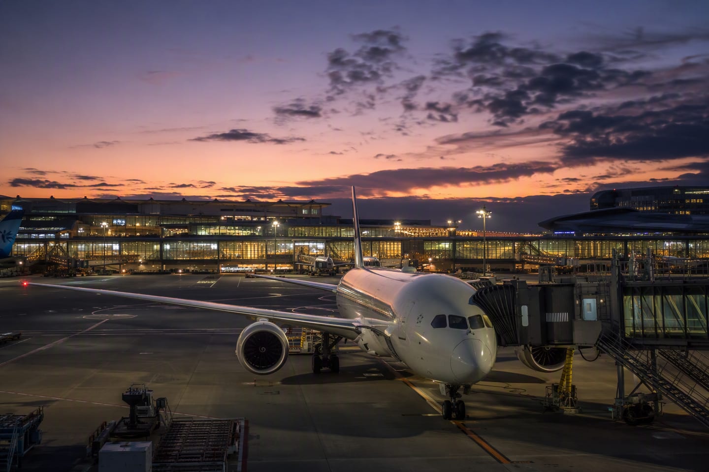 A wide-body Boeing 787 waits at the gate beneath the glowing departure halls of Tokyo Haneda Airport’s Terminal 3 at dusk.
